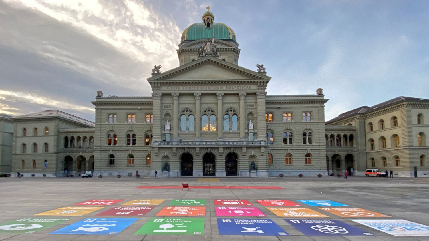 Une image du Palais fédéral avec la Place fédérale devant. Sur le sol de la Place fédérale, on peut voir les 17 ODD qui ont été collés sur le sol.